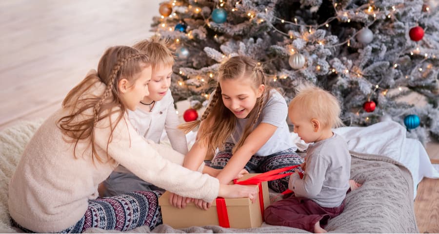Children opening a gift beside a Christmas tree.
